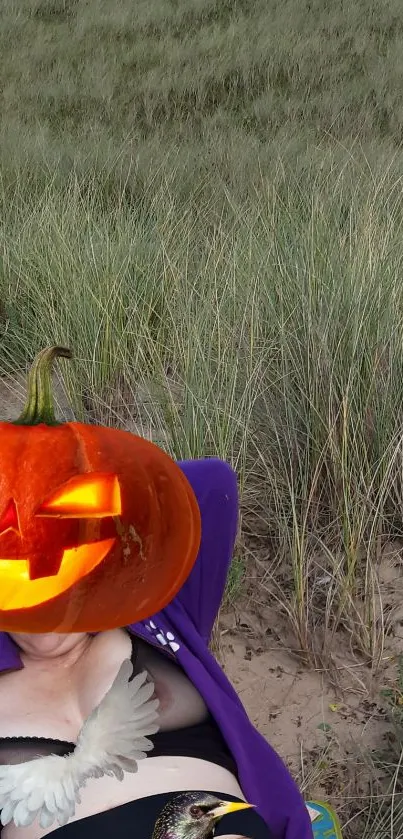 Halloween pumpkin head on beach with grasses in background.