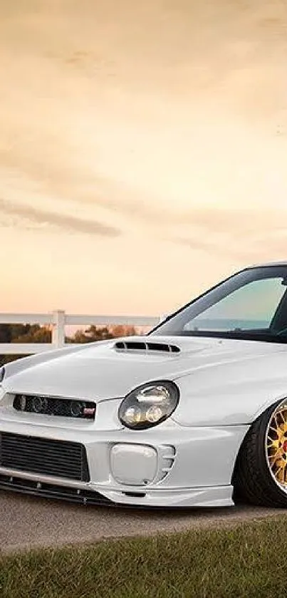 White sports car with gold wheels against a sunset backdrop.