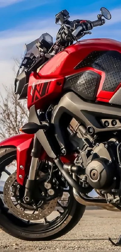 Red sport motorcycle parked on road against blue sky.