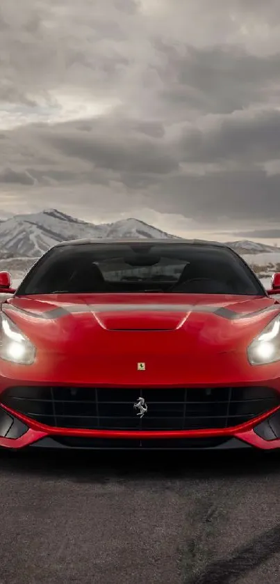 Red sports car on road with mountains and cloudy sky backdrop.