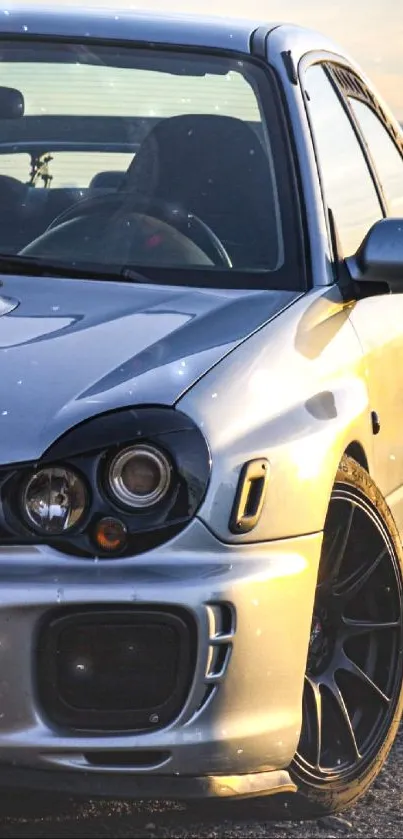 Sporty silver car at sunset with dark racing wheels and sleek design.