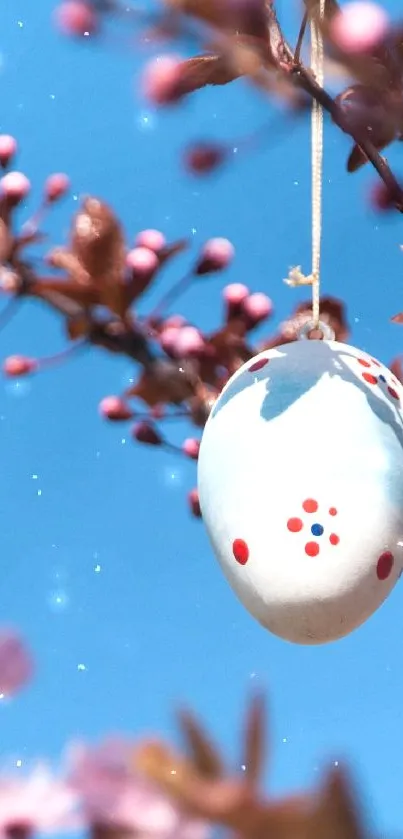 Egg decoration hanging on blossoming branch with blue sky background.