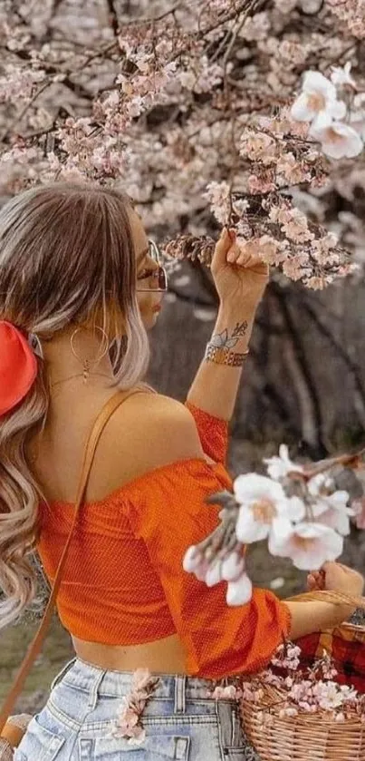 Woman in orange blouse under cherry blossoms in springtime.