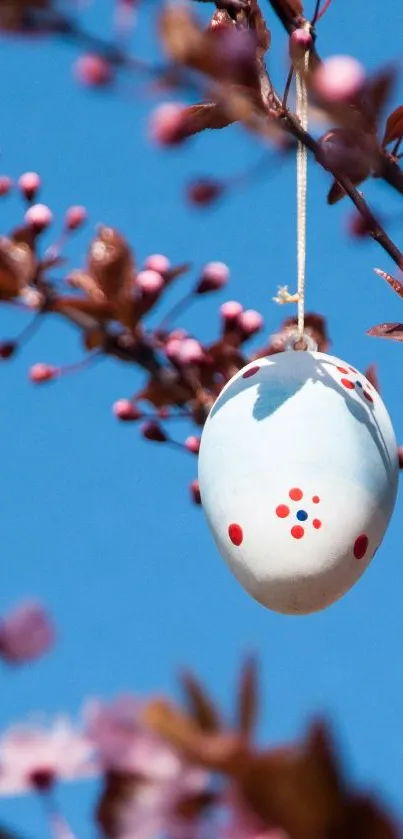 Decorative Easter eggs hang on blooming branches against a blue sky.