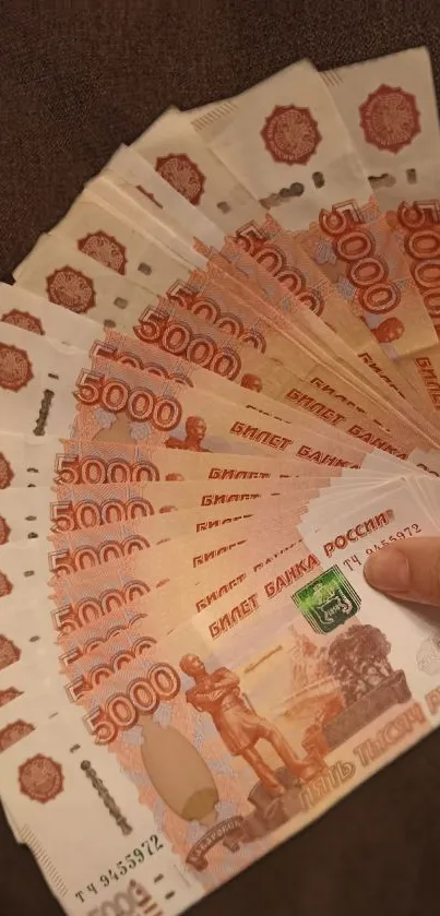 A fan of 5000 Russian Ruble banknotes on a mobile wallpaper.