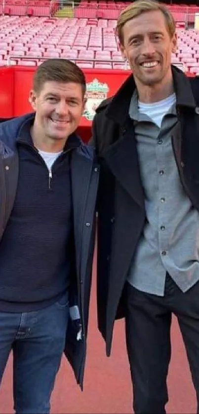 Two friends standing in a red stadium with casual outfits.