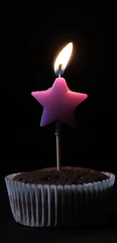 Pink star candle on chocolate cupcake in dark setting.