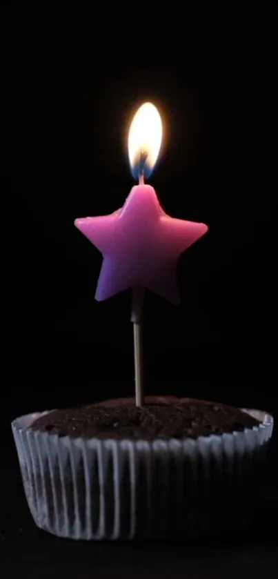 Pink star candle on a chocolate cupcake against a dark backdrop.