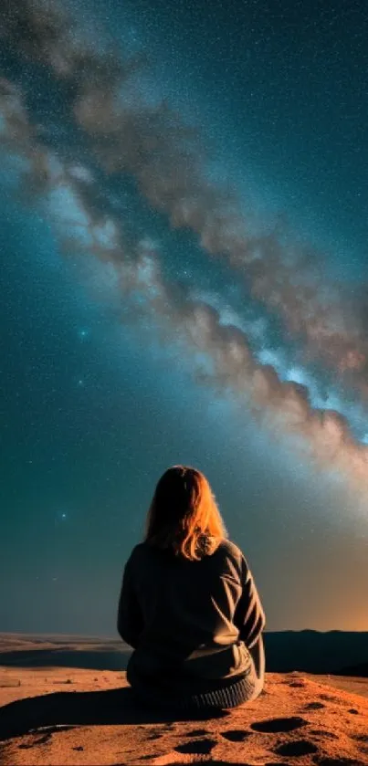 Person gazing at starry night sky in desert landscape.