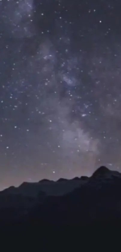 Starry night sky above dark mountain silhouette.