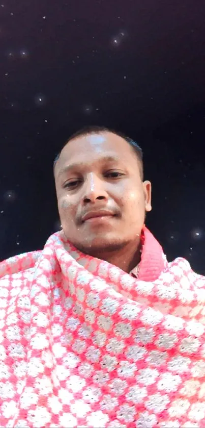 A man wrapped in a pink blanket under a starry night sky.