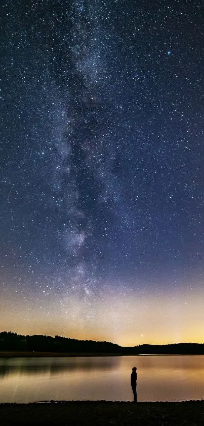 Silhouette under starry sky by calm lake, showcasing the Milky Way.