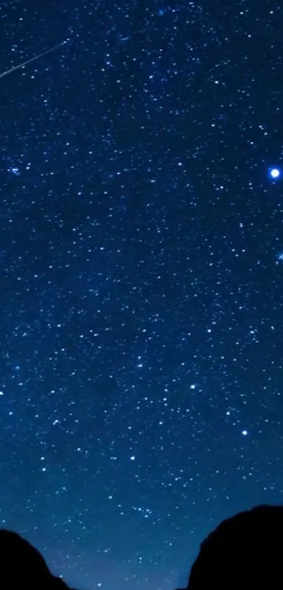 Starry night sky with shooting star over dark silhouette hills.