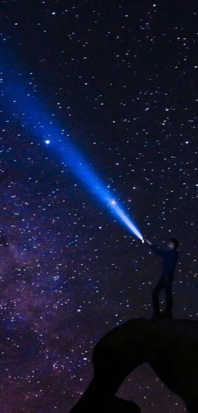 Silhouette on rock under starry night sky with flashlight beam.