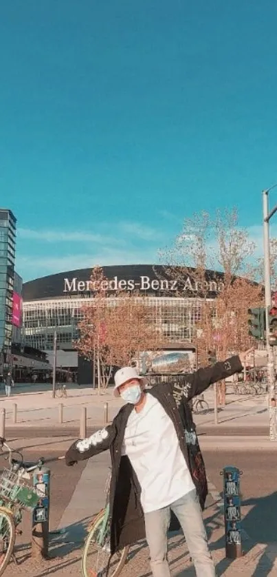 Man posing in city street under a blue sky with urban background.