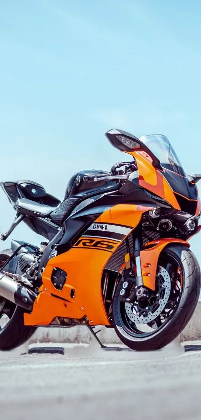 Orange motorcycle parked with a blue sky backdrop.