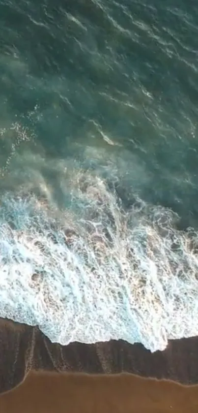 Aerial view of ocean waves crashing on a sandy beach with teal blue water.