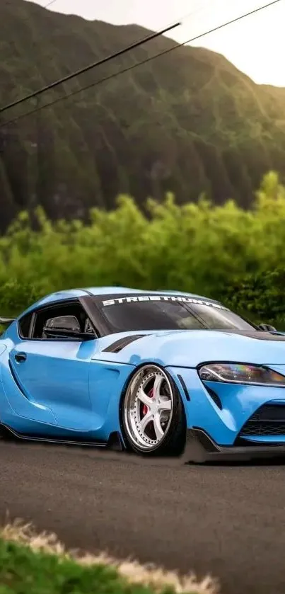 Blue sports car on scenic mountain road with greenery.