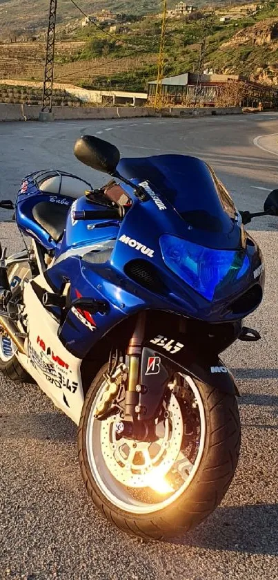 Blue Yamaha R1 motorcycle against a scenic sunset backdrop on a winding road.