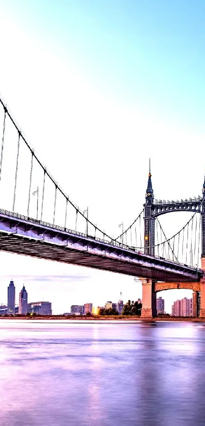 Suspension bridge over river at sunset with city skyline.