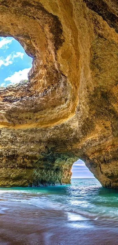 Sunlit coastal cave with sandy beach and turquoise ocean.