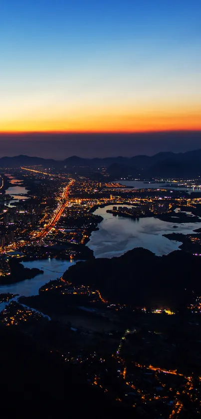 Aerial view of coastline city at dusk with glowing city lights and colorful sunset sky.