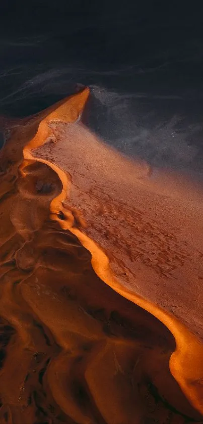 Aerial view of orange sand dune in desert landscape with dark sky backdrop.