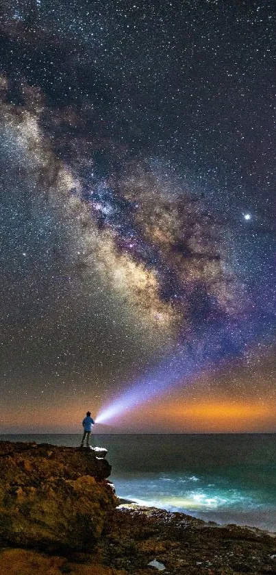 Person at ocean cliff under a vibrant Milky Way night sky.