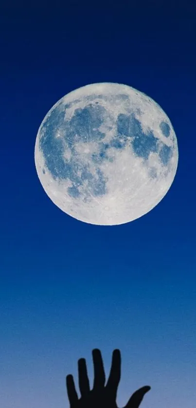 Hand reaching for the full moon in a dark blue sky wallpaper.