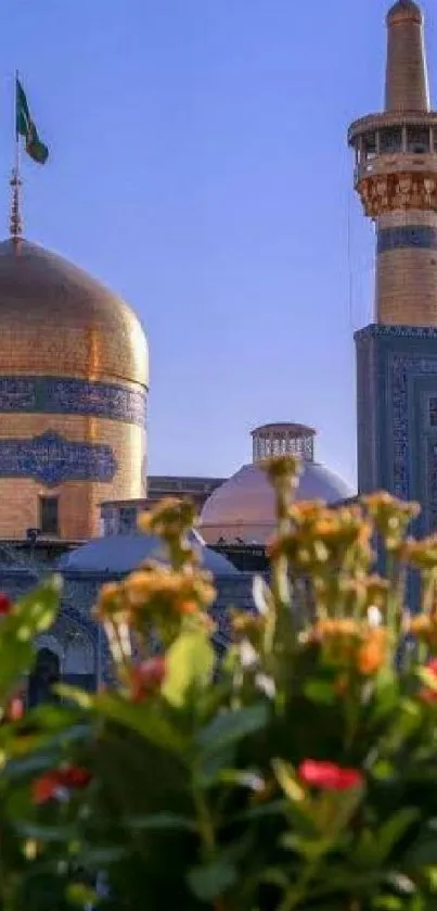 Golden domed mosque with flowers and clear blue sky.