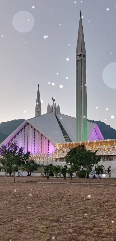 Mosque at dusk with colorful lighting and mountains in the background.