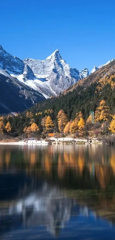 Scenic mountain lake with snowy peaks and autumn trees under a blue sky.