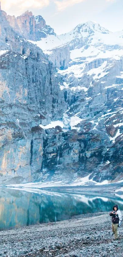 Snow-capped mountains reflected in a calm lake with a serene rocky shoreline.