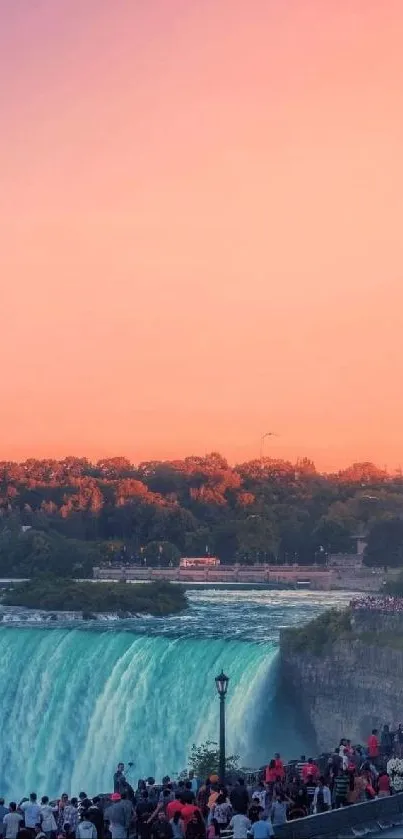 Niagara Falls at sunset with pink sky and tourists viewing the scene.