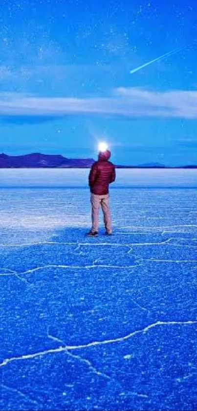 Person under a starry sky on salt flats with vivid blue hues and distant mountains.