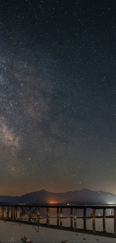 Starry night sky over mountains with a bridge in view.