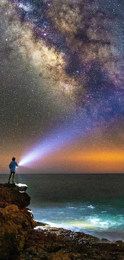 Person on cliff under Milky Way night sky with ocean view.