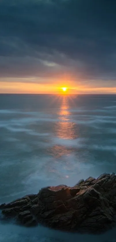 A breathtaking sunset over a calm ocean with a rocky shore in the foreground.