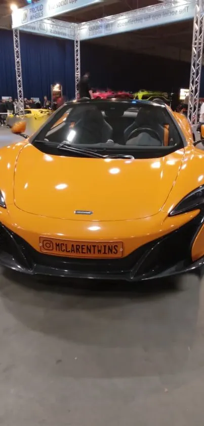 Orange sports car displayed at an indoor auto show.