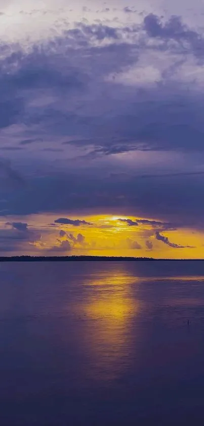 Purple sunset over calm water with reflection under a cloudy sky.