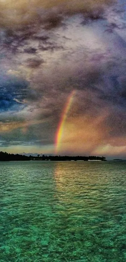 Vibrant rainbow over serene ocean waters with cloudy sky backdrop.