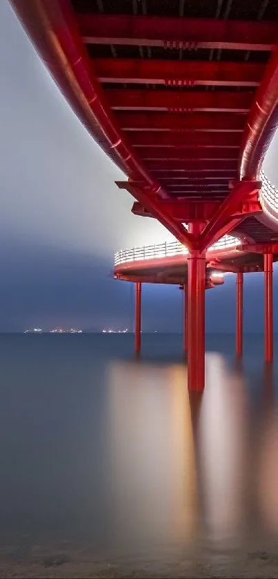 Red bridge extends over calm sea under a gradient sky.