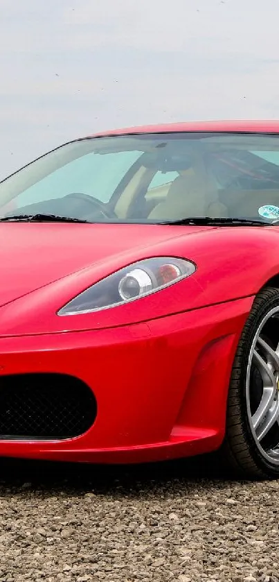 Red sports car on gravel road with sleek design features.