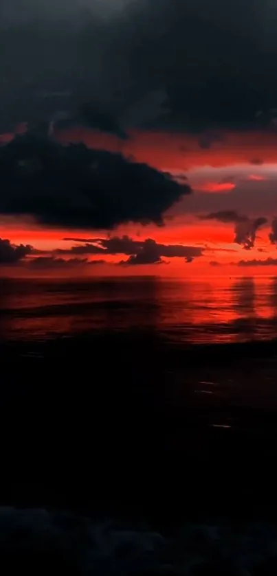 A breathtaking red sunset over a tranquil ocean horizon with dark clouds.