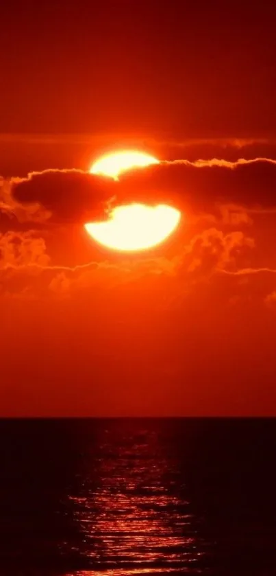 Vibrant red sunset over ocean with clouds and reflection.