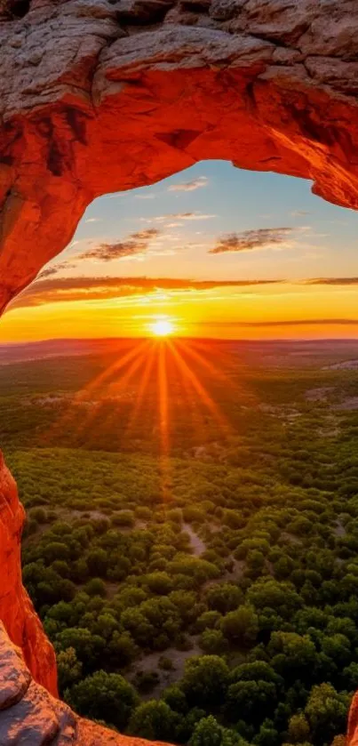 Vibrant sunset through a rocky arch over lush landscape.