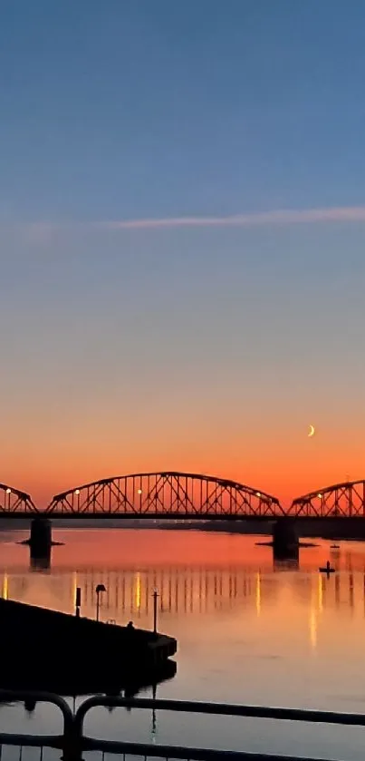 Sunset over silhouetted bridge with serene water reflections.