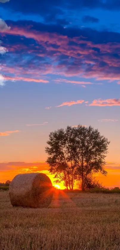 Serene field with hay bale and sunset sky in vibrant hues.