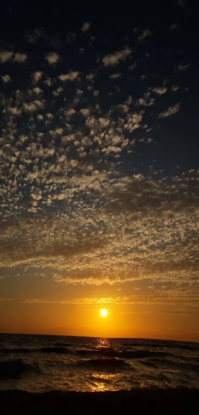 Golden sunset over ocean with clouds and waves on horizon.