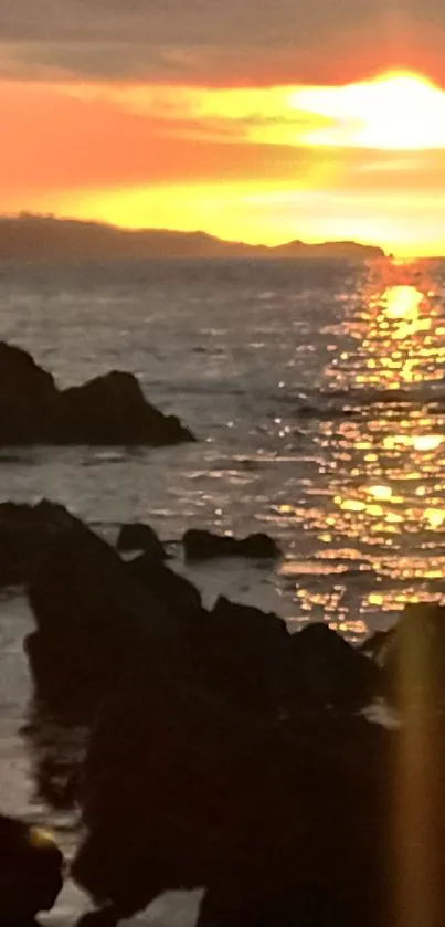 Sunset over rocky ocean shore with vibrant colors.